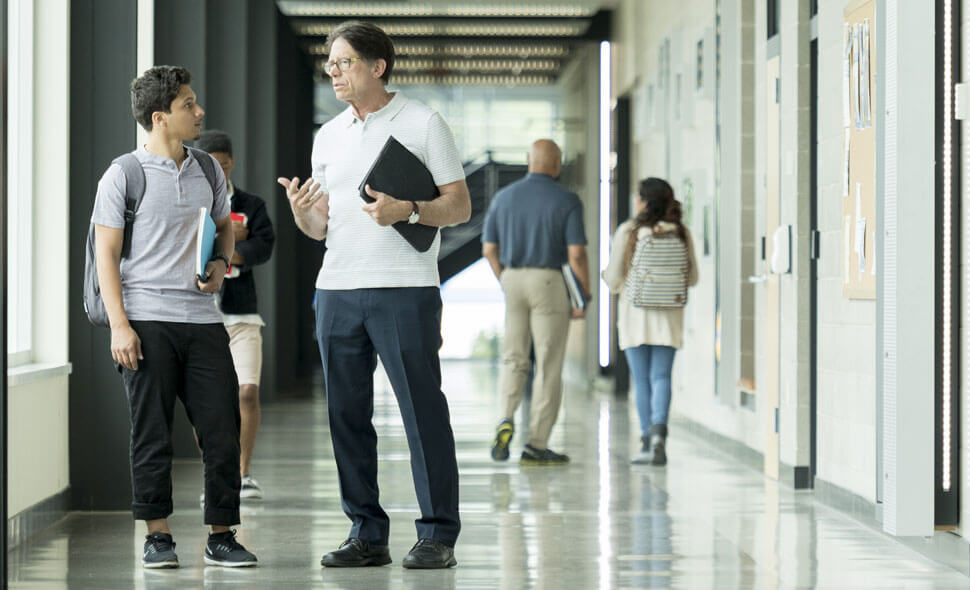 Student and school faculty member having a discussion in a brightly lighted college hallway