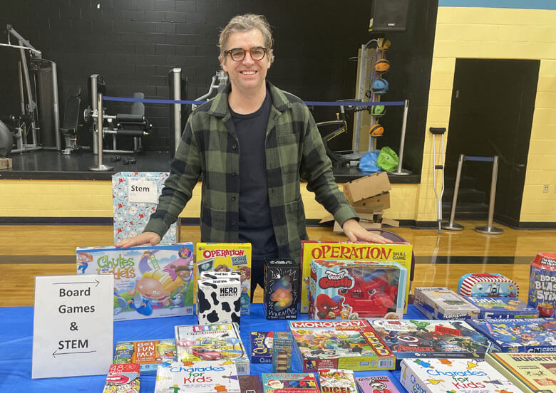 A man is standing behind a table covered with toys and games