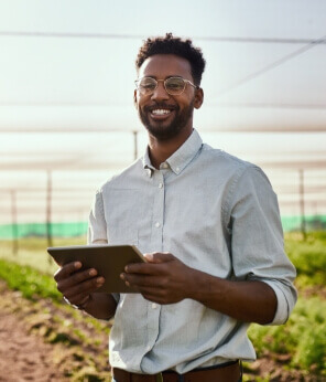 Young black man holding a tablet standing in a modern farm field