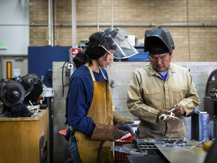 Teacher and student together working in a shop and wearing protective head gear