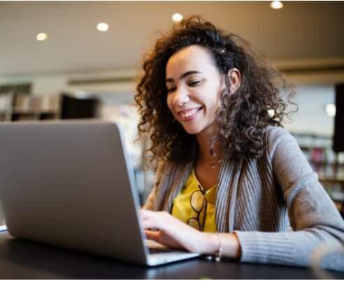 Young black woman smiling and sitting in a public space in front of laptop