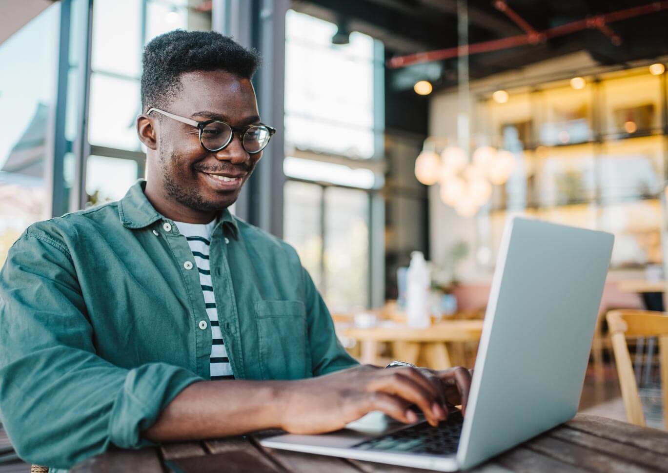 Young black man smiling and working at a laptop in a public space