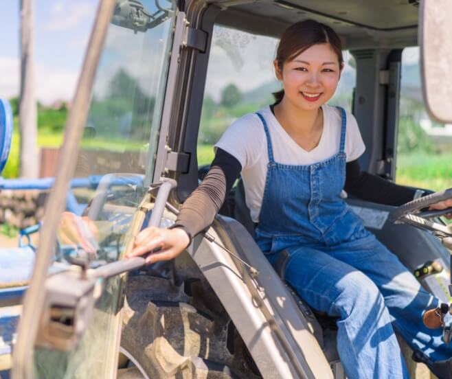 Young woman in overalls siting in a tractor outside on a sunny day
